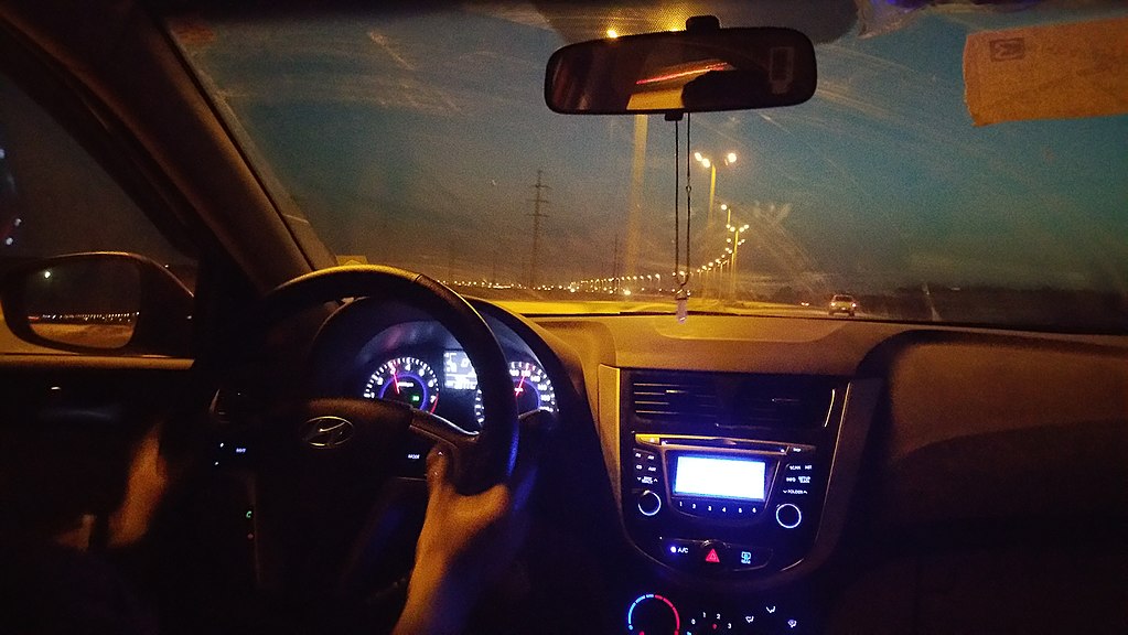 A photograph of the interior view through the windshield of a car at night.