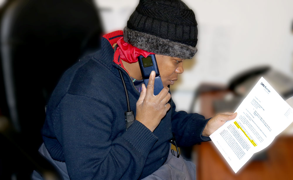 Kitty, a Street Sense Vendor, sitting at a desk, talking on the phone and holding a legal notice that she needs to provide more paperwork to keep her subsidized housing in good standing.