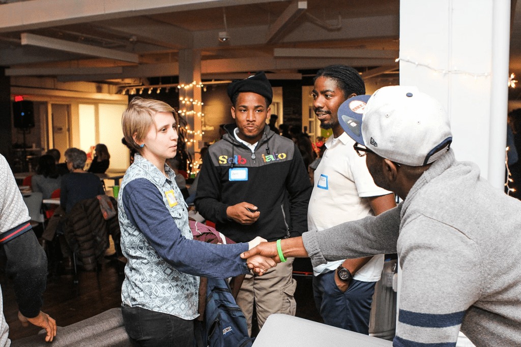 A photo of a woman and a man shaking hands at an event while two other men with name tags stand by.