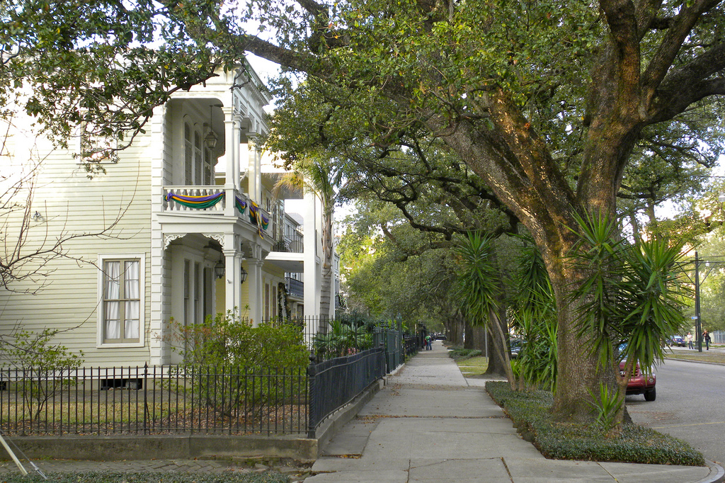 Photo of a large house in the Garden District on a nice tree-lined street with Mardi Gras banners hanging from the railing of an upper balcony.