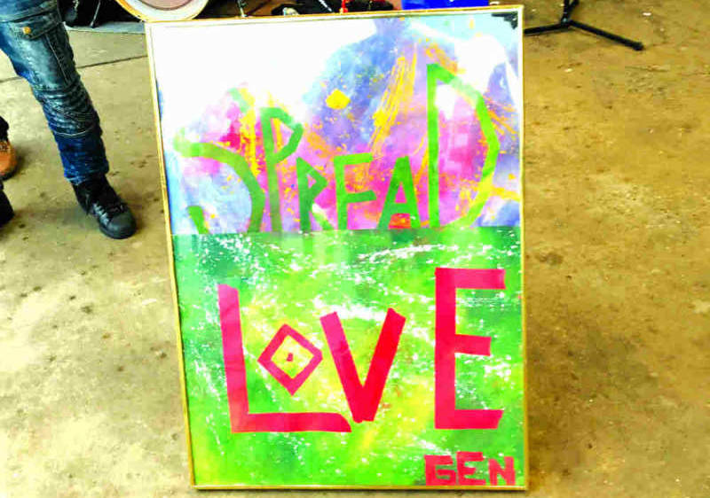 Color photo of a painted board that reads "Spread Love" in fron of a drum kit