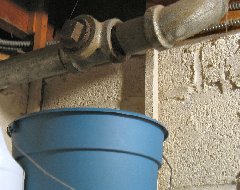 Photo of a pipe with a bucket catching water.