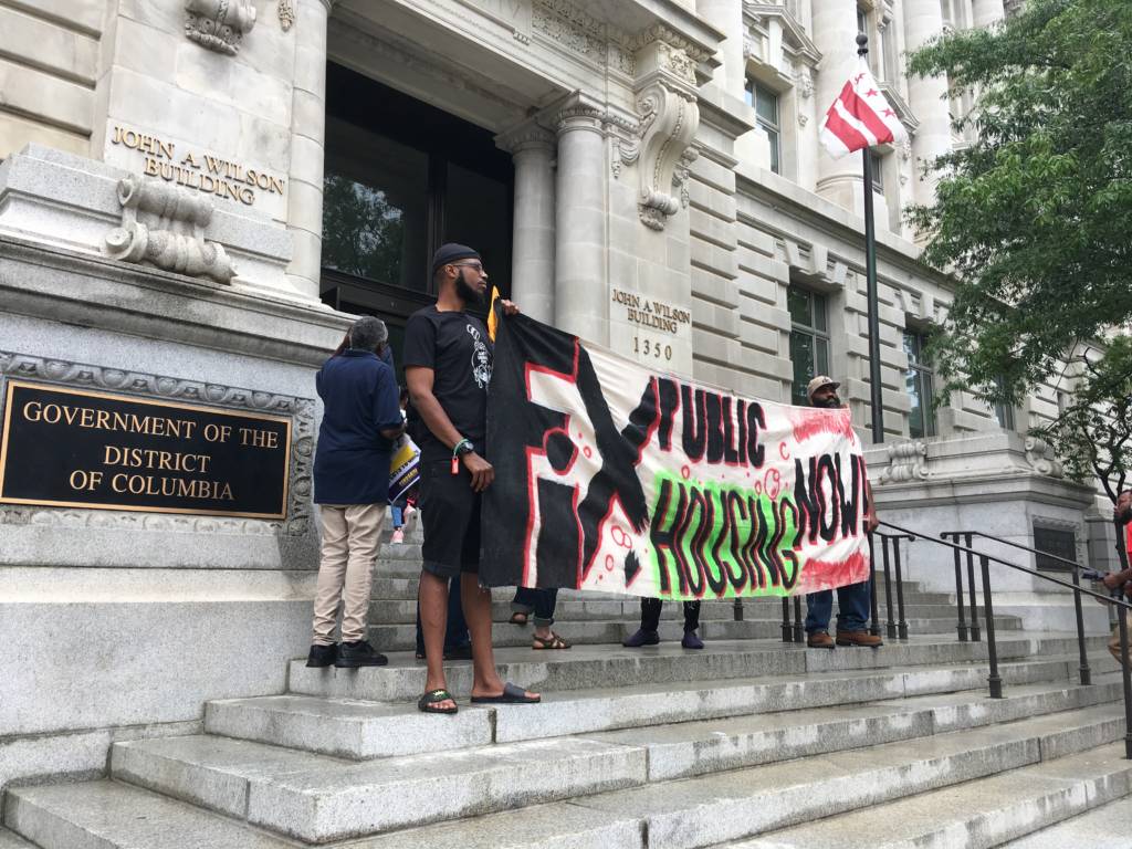 Photo of activists holding a sign stating "fix public housing now"outside the DC Council on May 28.