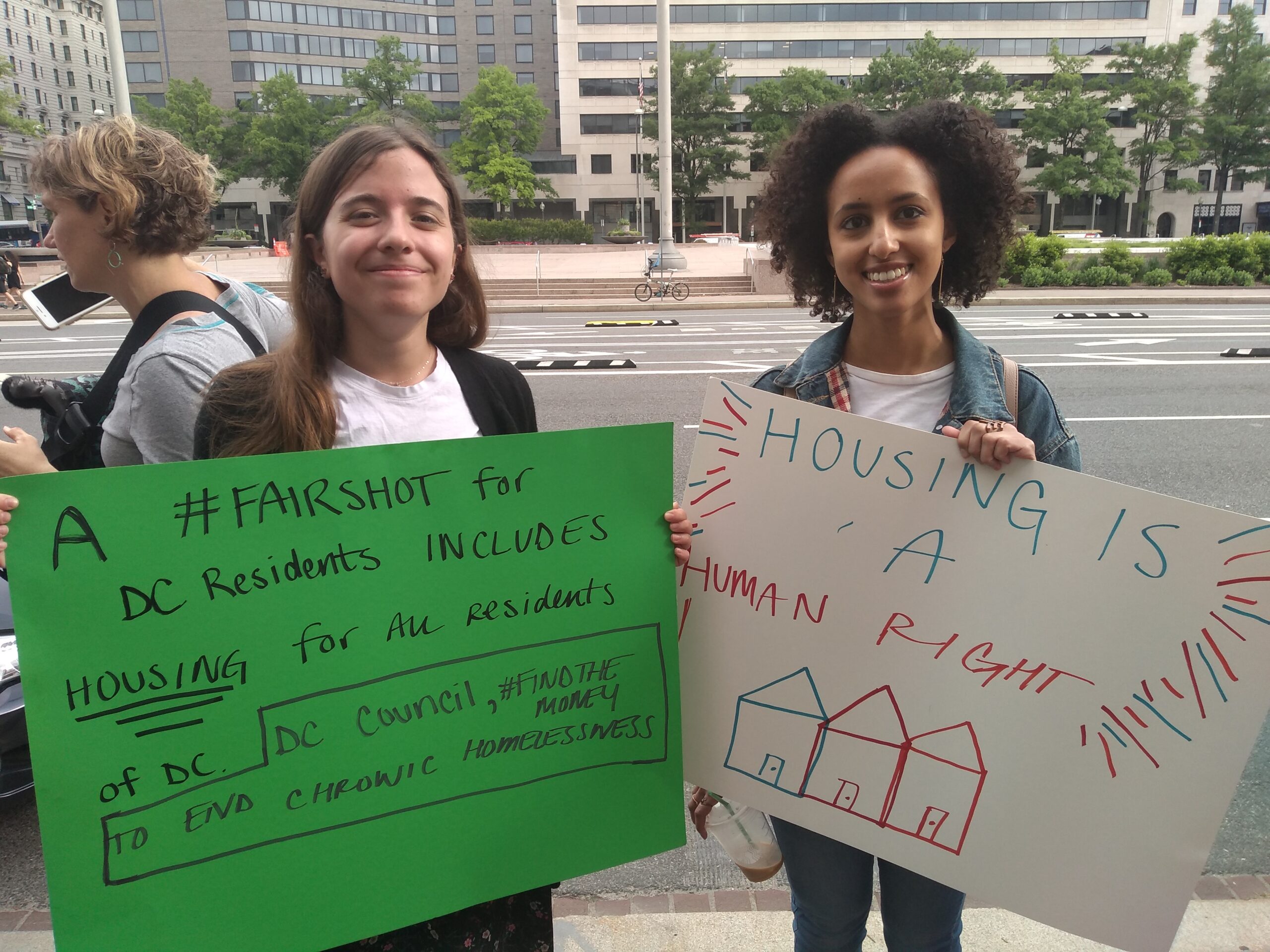 Photo of two advocates holding signs saying "A #FAIRSHOT for DC residents includes housing for all residents" and "Housing is a human right."