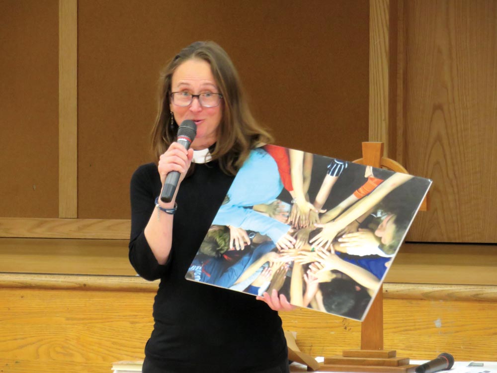 Photo of Rev. Dunfey holding a printed and blown up photo of many hands reaching in to all touch as one.