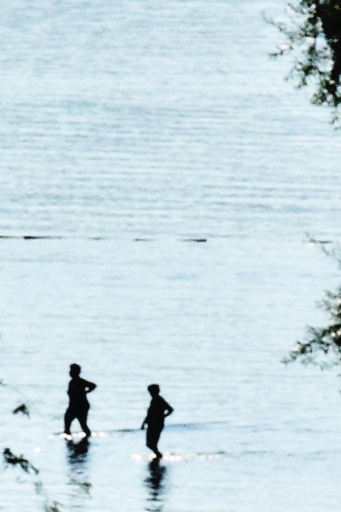 A photo showing two people walking in the water.