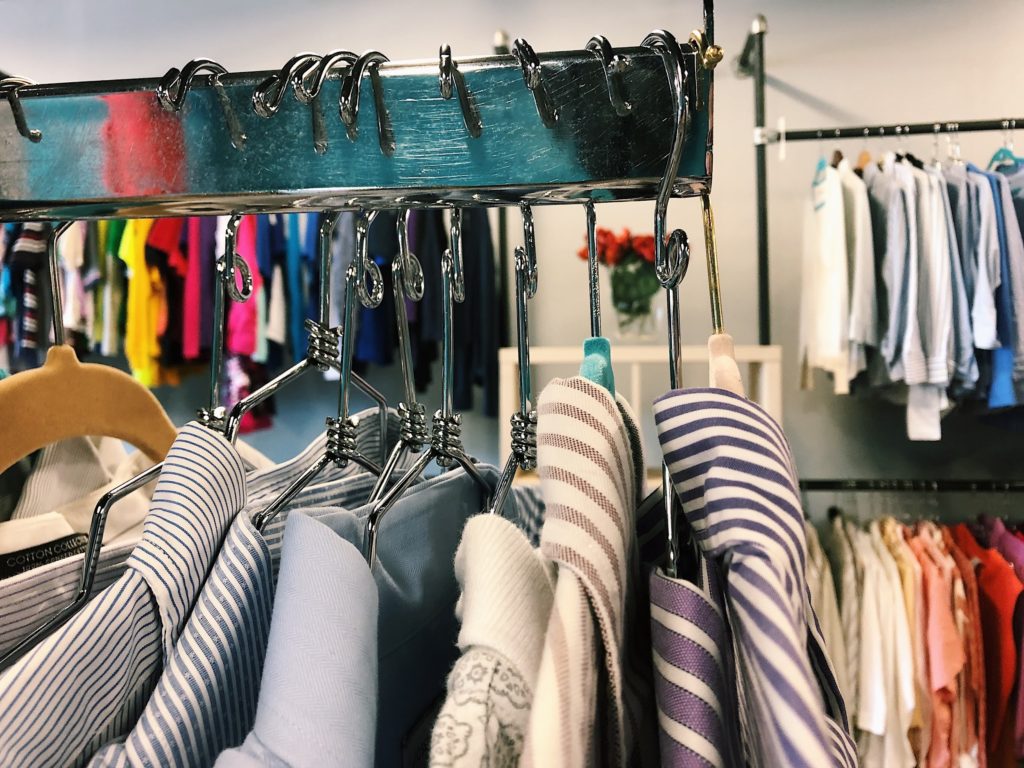 Photo of a row of dress shirts on hangers with a brightly colored wall of other clothes in the background.