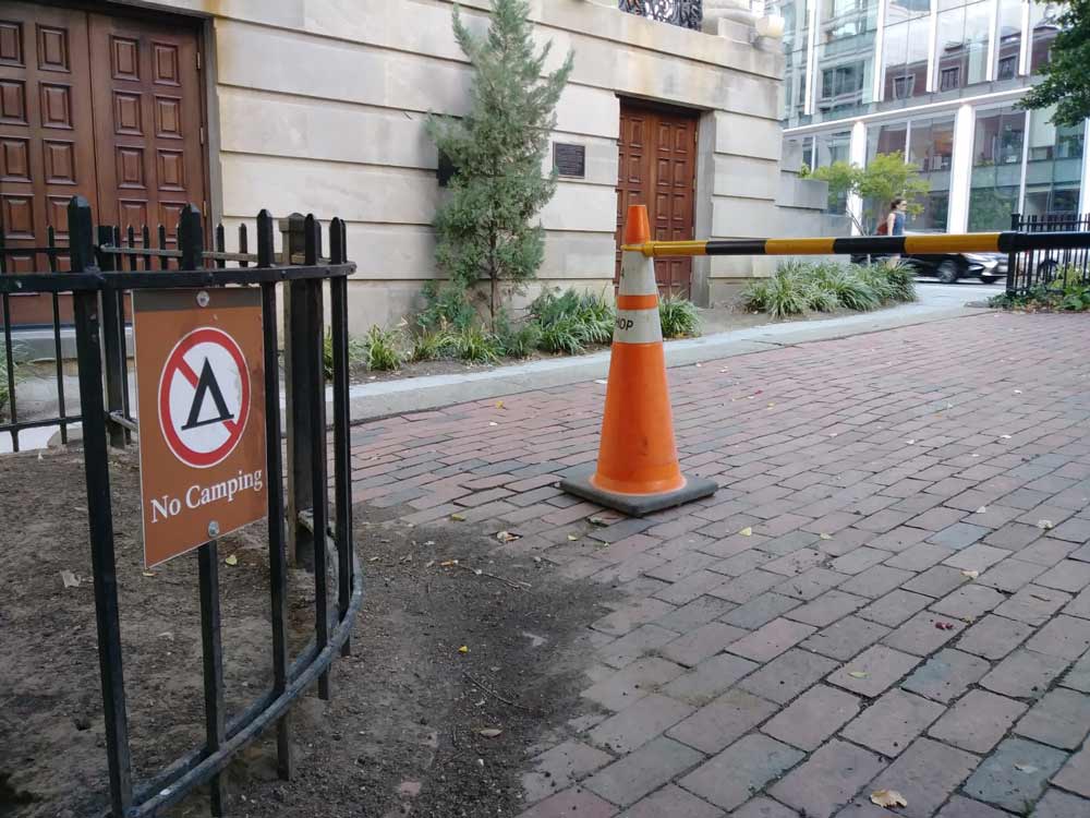 Photo taken outside on New York Avenue showing a cone with caution tape and a sign that says no camping.