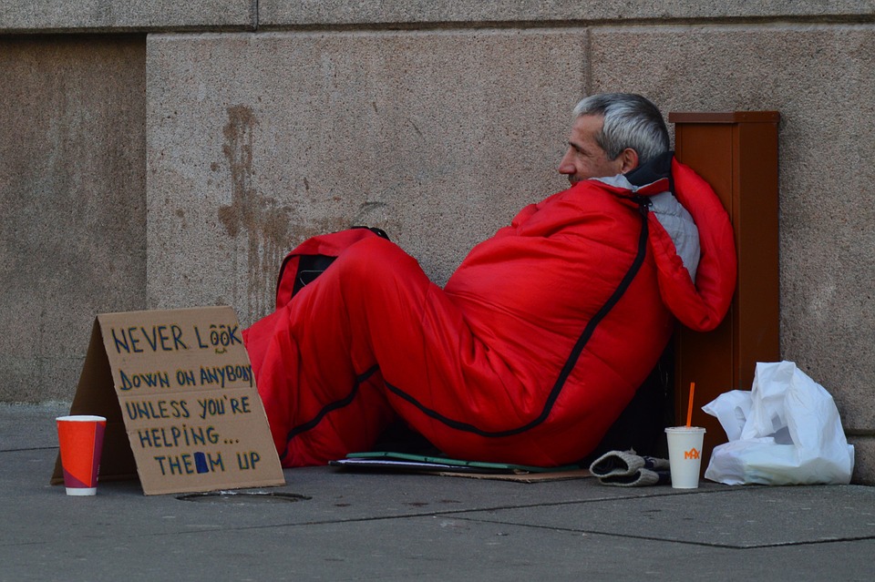 Homeless man sitting on the sidewalk with a cardboard sign.