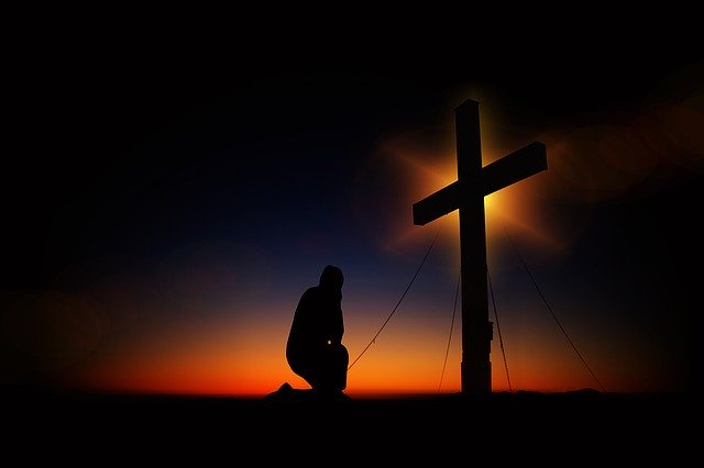 Image of a man praying in front of a cross at sunset.