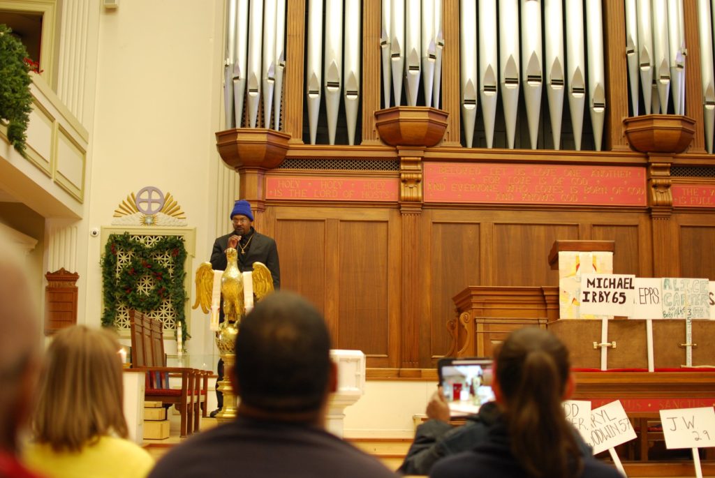 An African-American male speaks behind a podium as congregants listen from the pews.