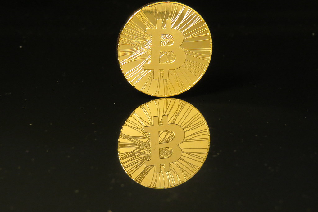 A shiny gold coin with the letter B on it sits on a black background.