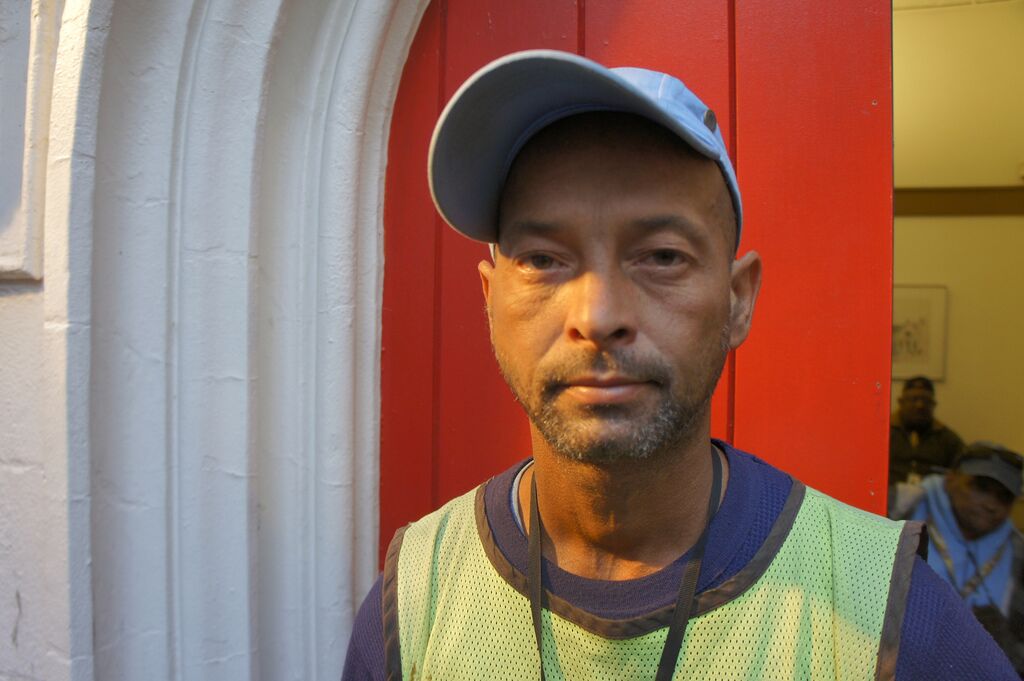 A man wearing a baseball cap and a Street Sense vendor shirt looks at the camera.