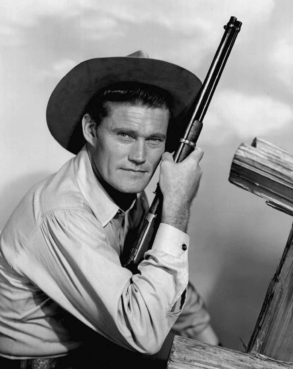 Actor Chuck Connors wears a cowboy hat and rifle and stares into the camera.