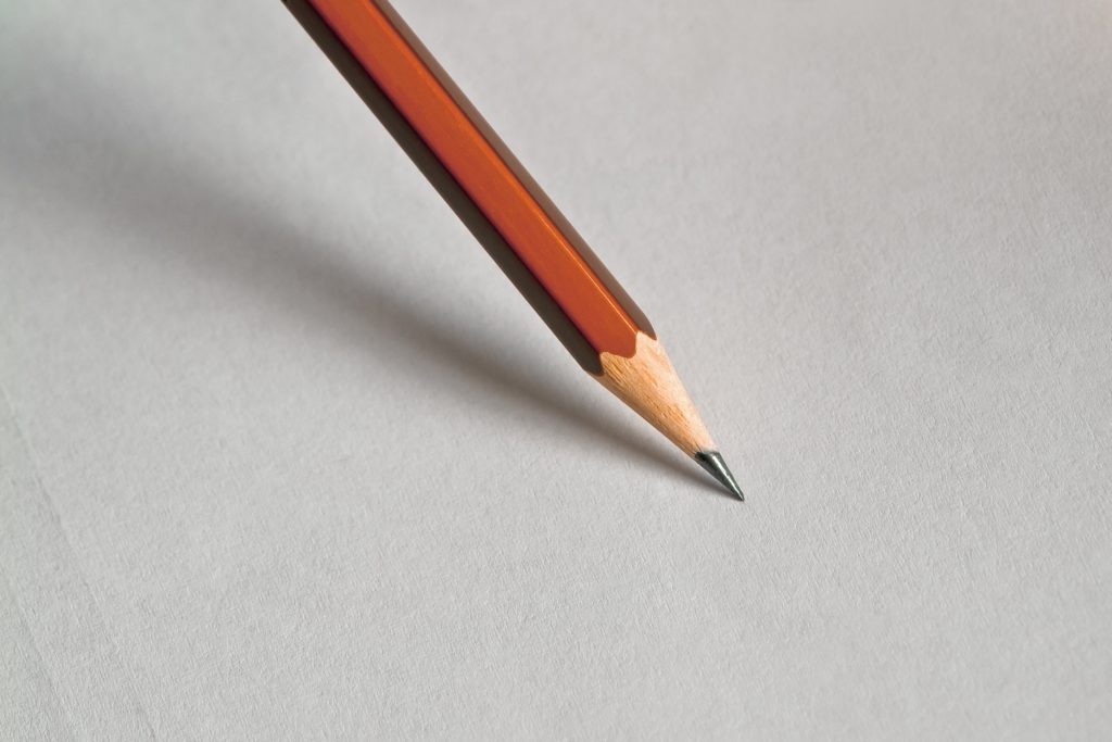 The tip of a pencil sits on white paper, ready to write.