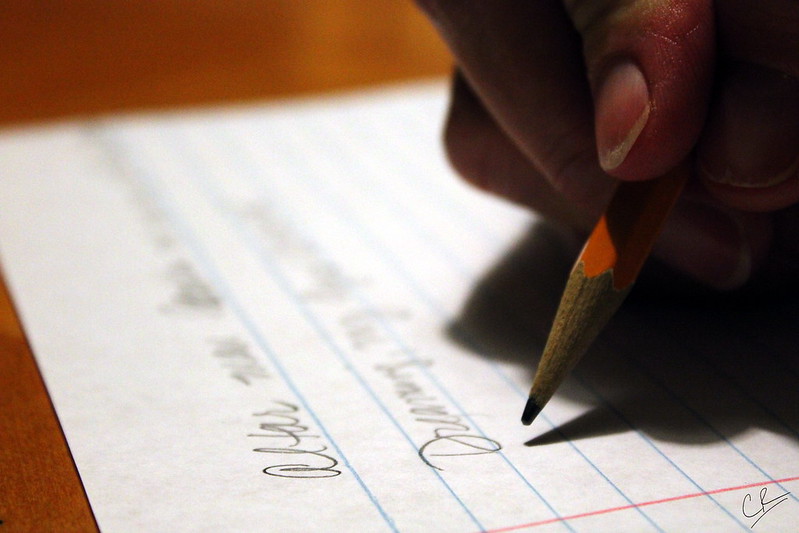 Photo of a hand holding a pencil above a sheet of notebook paper with two lines already written.