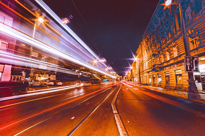 A photo of a city street. Car lights streak across the photo