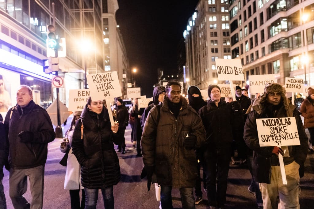 A group of people wearing winter coats holding signs on as they walk on a D.C. street at night