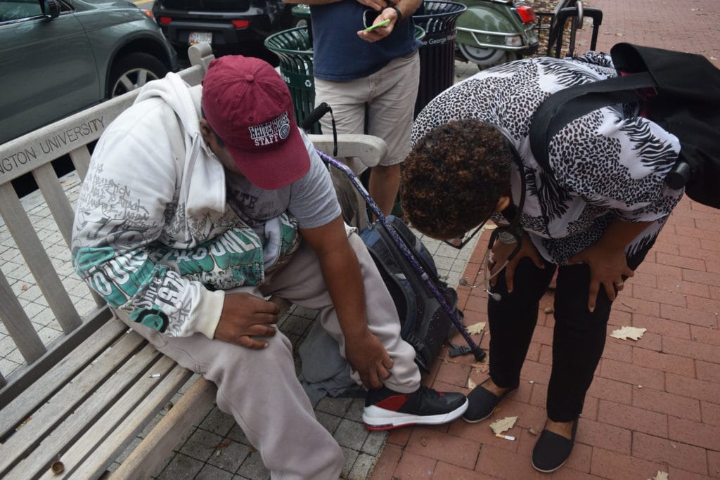 A woman helps out a homeless resident sitting on a bench.