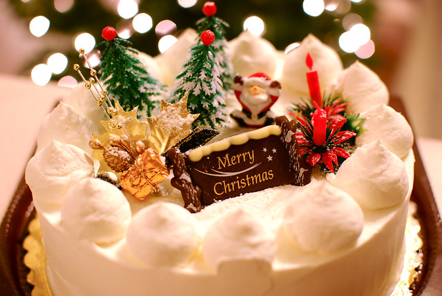 A cake depicting Santa Claus, a wreath, candles, and three Christmas trees.