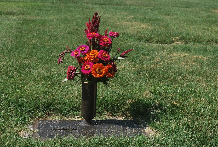 A vase holding red and orange flowers sits atop a grave.