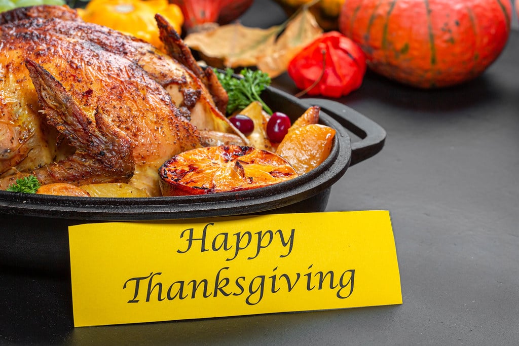 A yellow sign saying Happy Thanksgiving rests against a black dish holding a cooked turkey