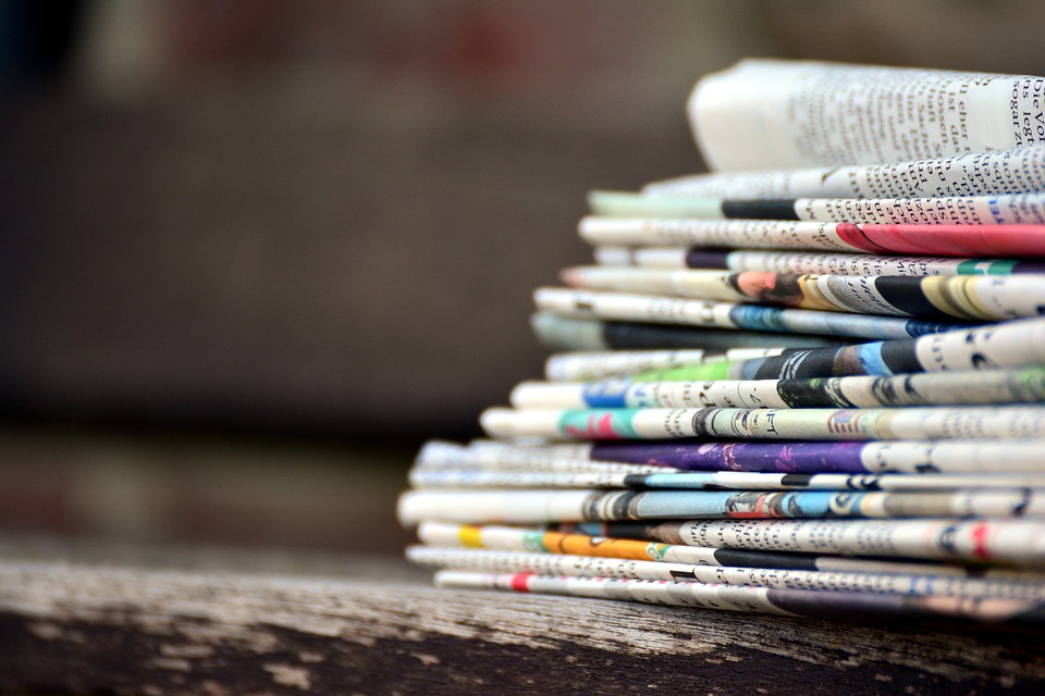 A stack of newspapers, a sliver of each front page's colored photo is visible in the stack.