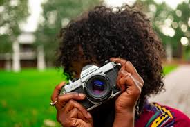 Photo of a black woman holding a camera in front of her face as she takes a photo.