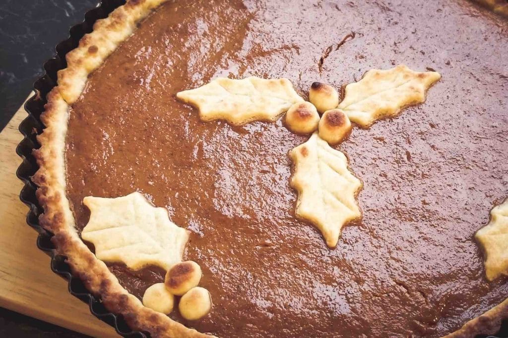 A close-up photo of a pumpkin pie. It has leaves made out of pie dough on top of the filling