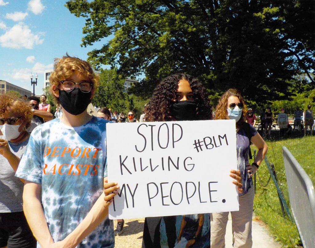 Photo of Black woman holding a sign that says "Stop killing my people"