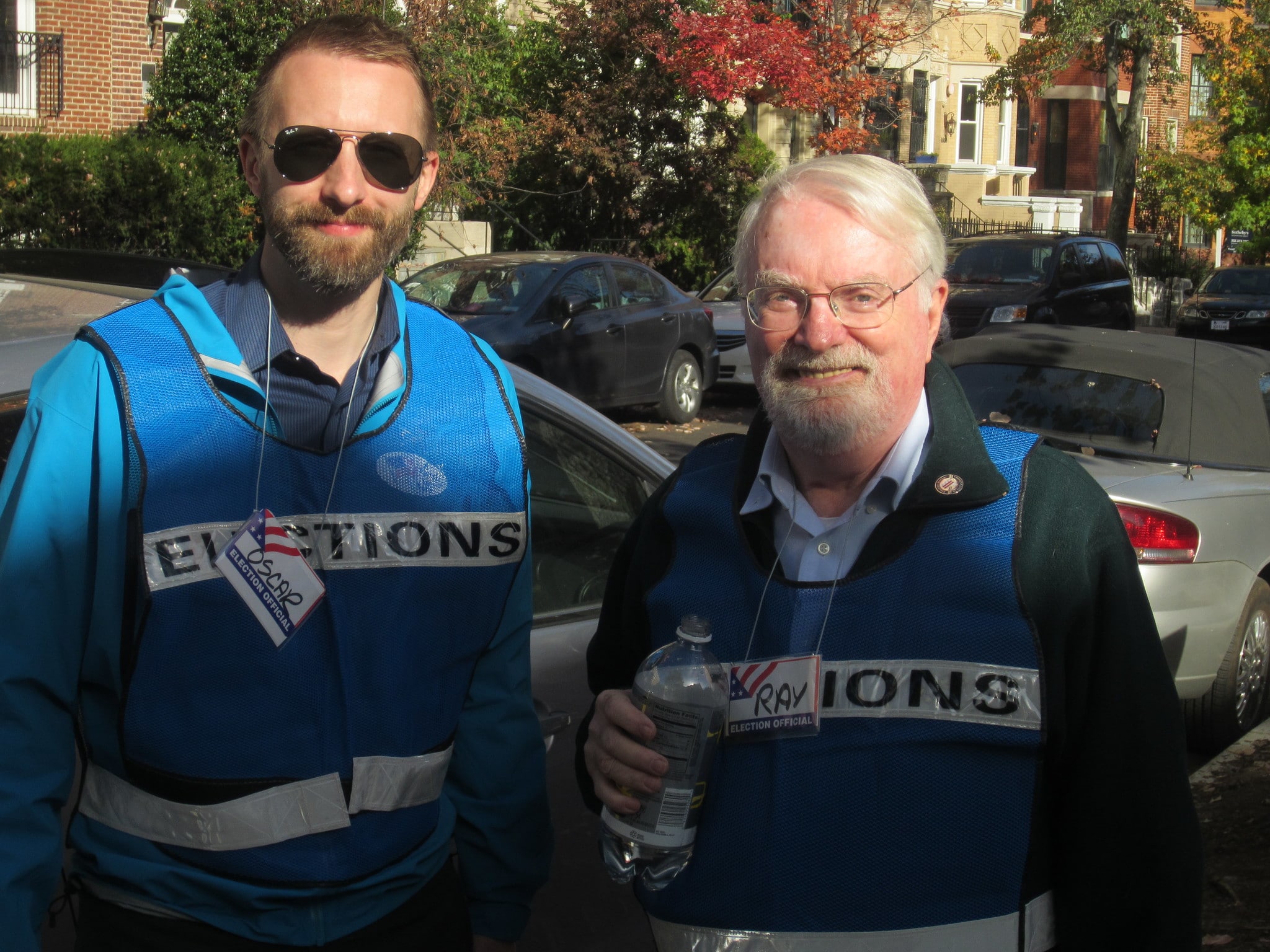 Photo of two men wearing blue vests that say "elections" on them.