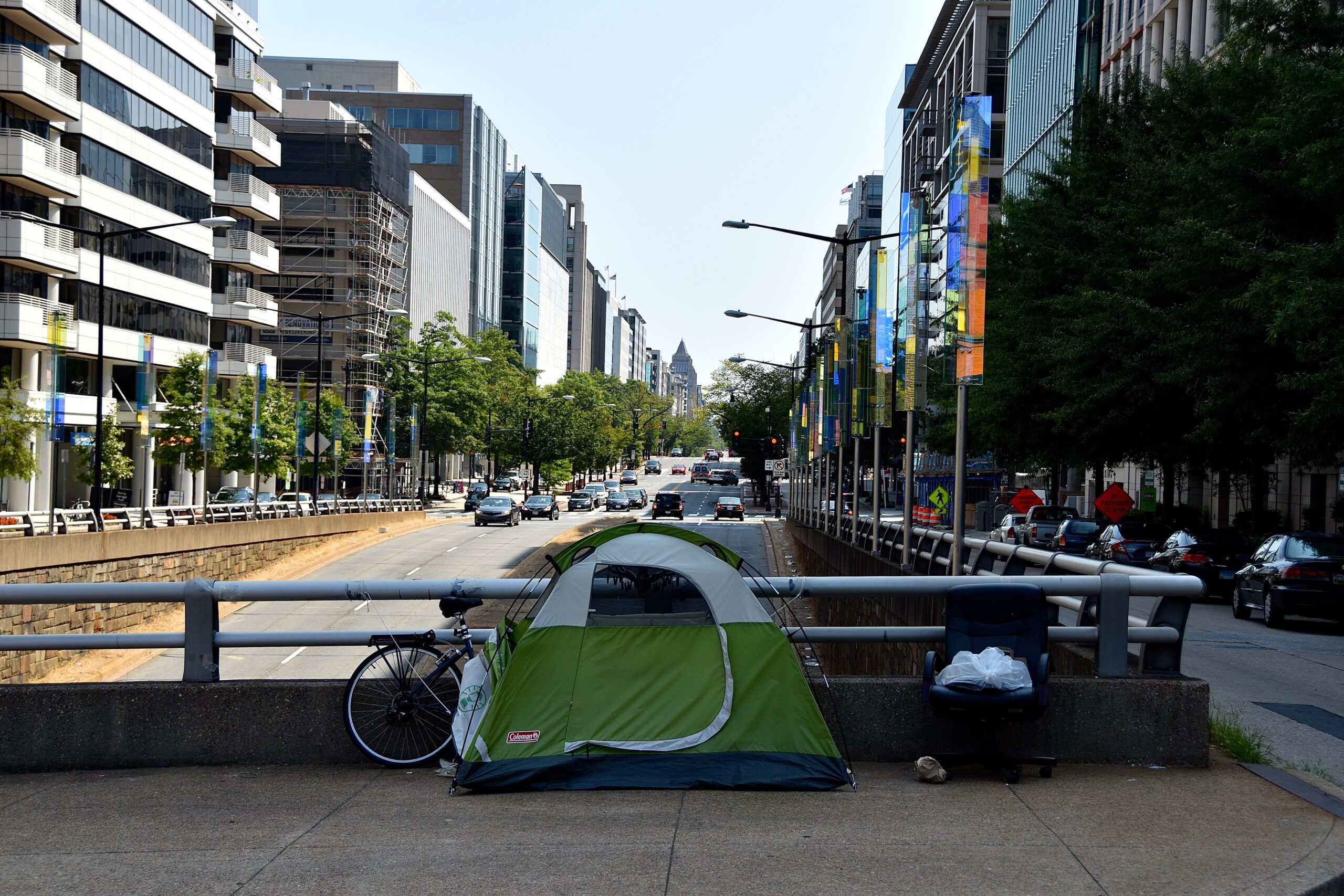 Photo of a green tent with a bike next to it a busy road on a passageway in front of a busy road in D.C.