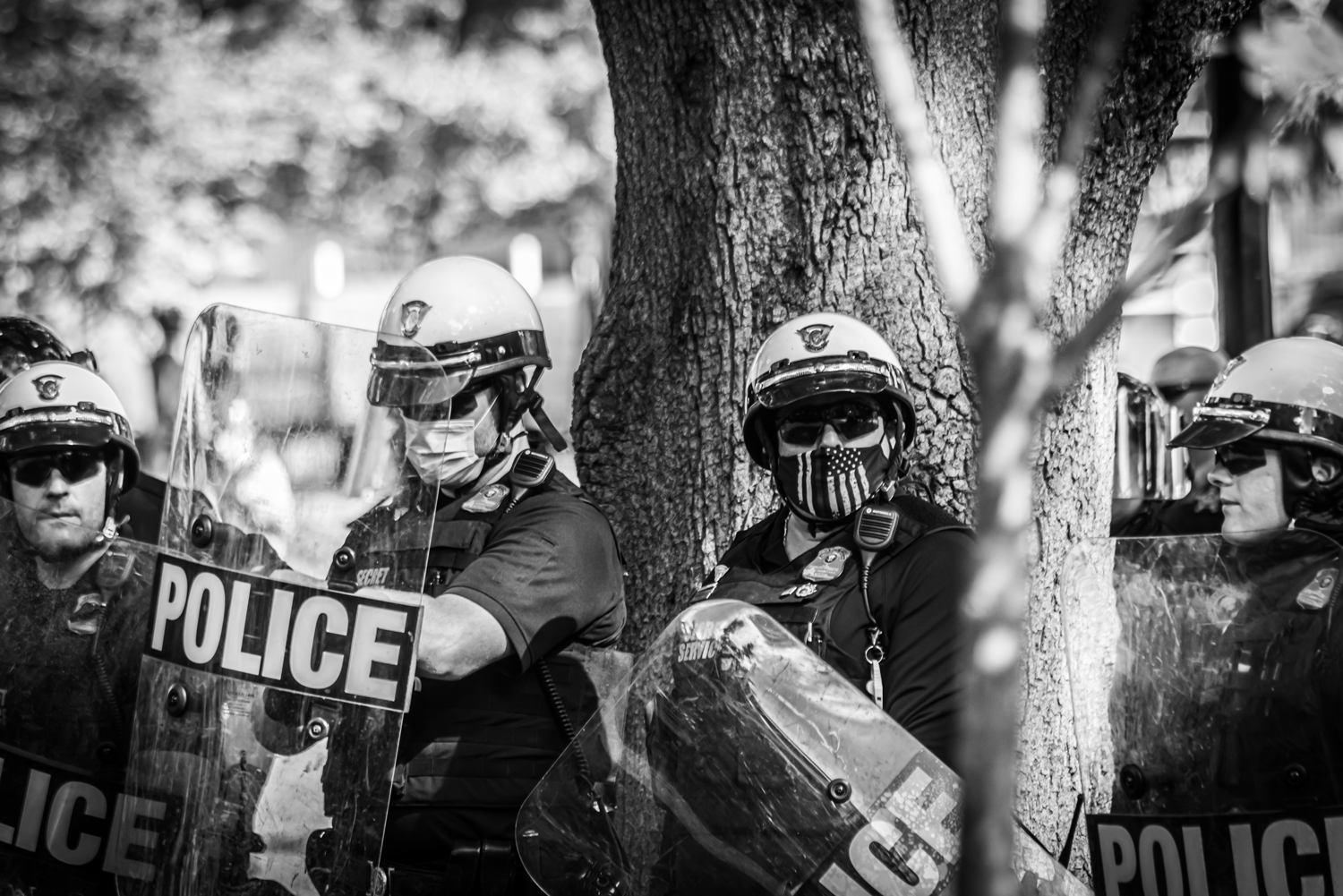 Black and white photo, both officers are wearing PPE also. One is staring straight at the camera.