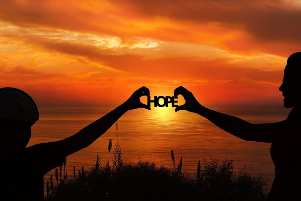 Sunset in the background, silhouette of two people joining hands with the word "hope" in the middle