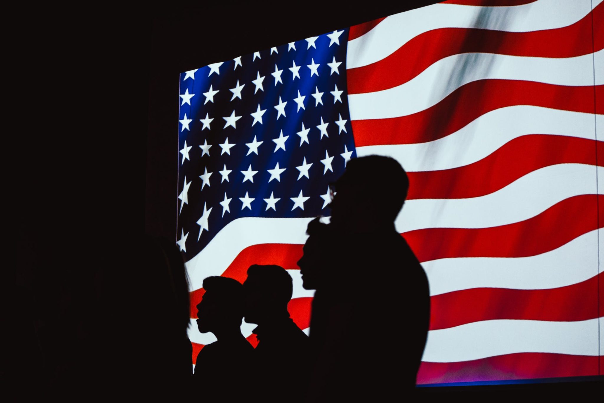 Photo of American flag with silhouettes of people standing in front of it.