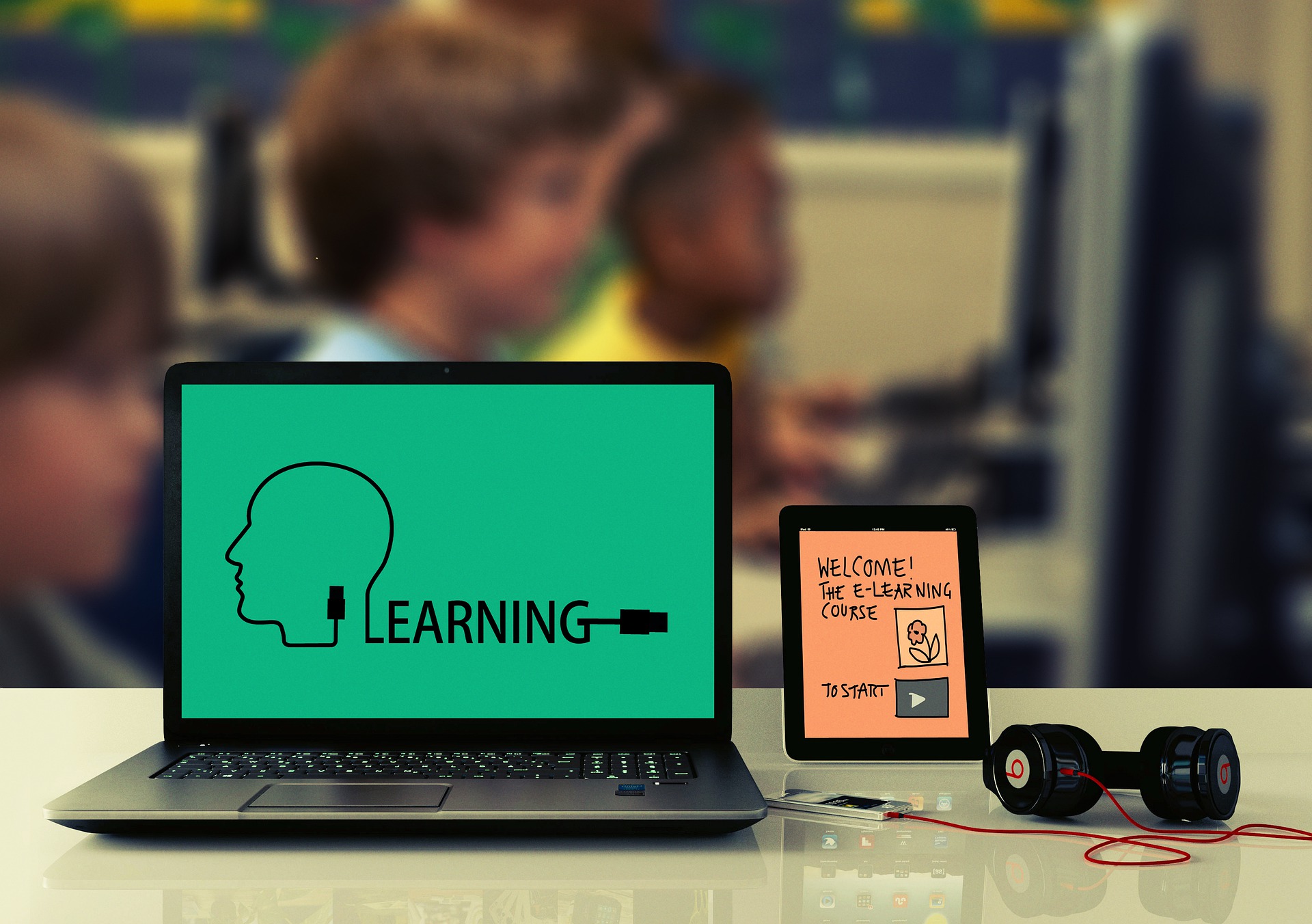 Photo showing a laptop that says "learning" on the screen with students out of focus in the background