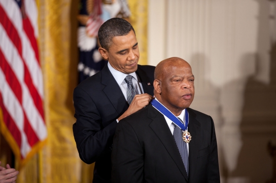 Obama stands behind Lewis, putting a medal around his neck.