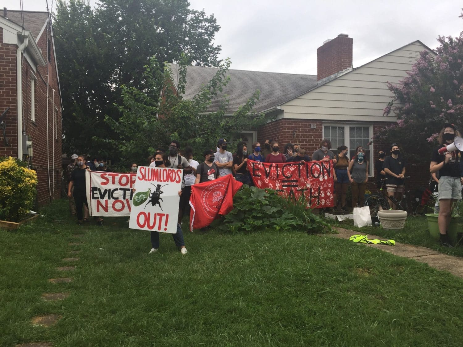 Photo of advocates standing and holding banners in a patch of grass outside of a residential building in Chillum, MD.