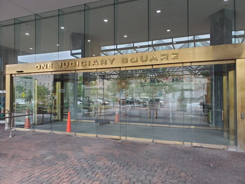 Photo showing a glass and bronze entrance with the words "one judiciary square"