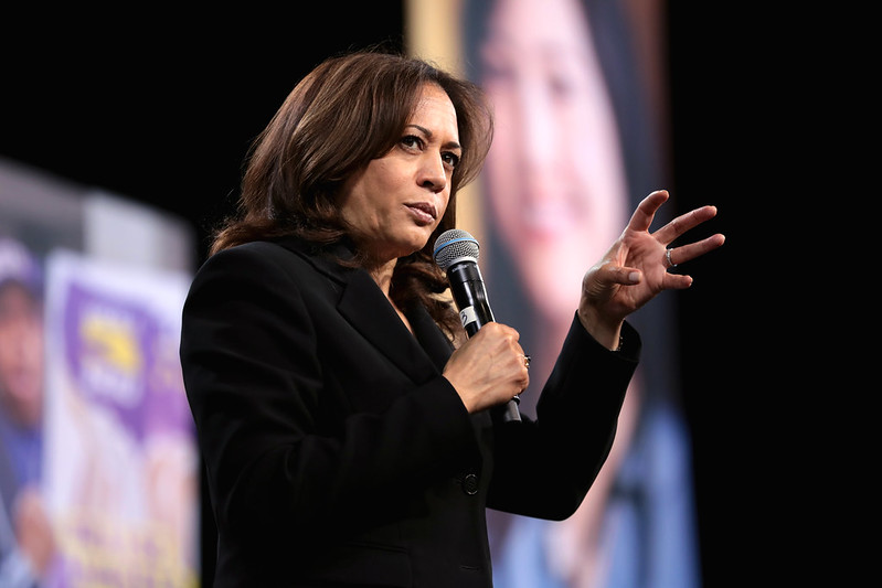 Kamala Harris speaks on a stage in front of a collection of photos.