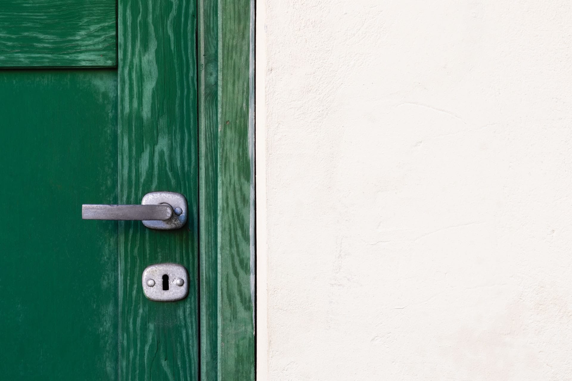 A door handle on a green door set against a white wall.