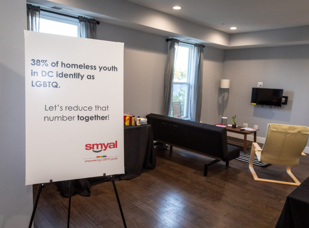 A sign in a living room reads "38% of homeless youth in D.C. identify as LGBTQ+. Let's change that number together."