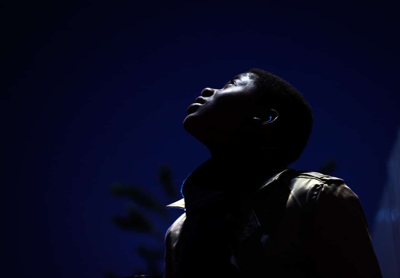 A Black man looks up at a dark blue light.