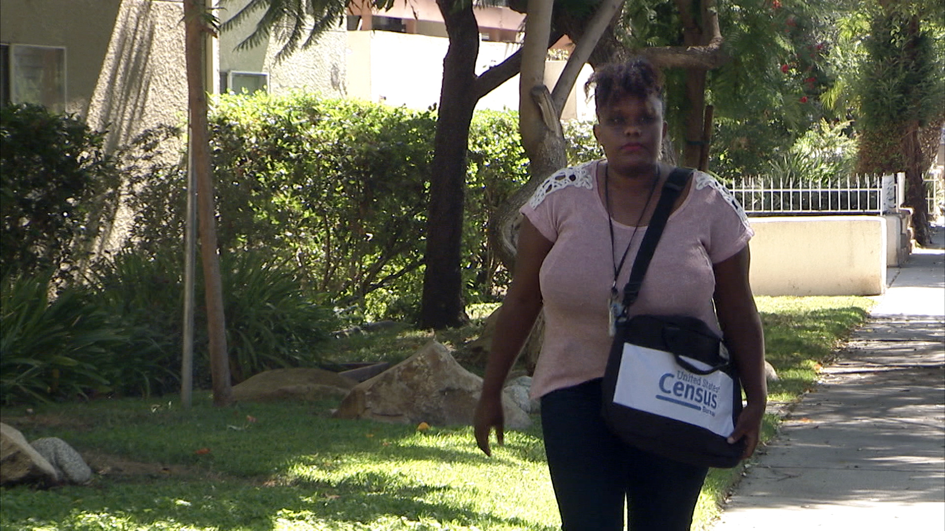 A woman walking next to a green lawn with a Census bag.