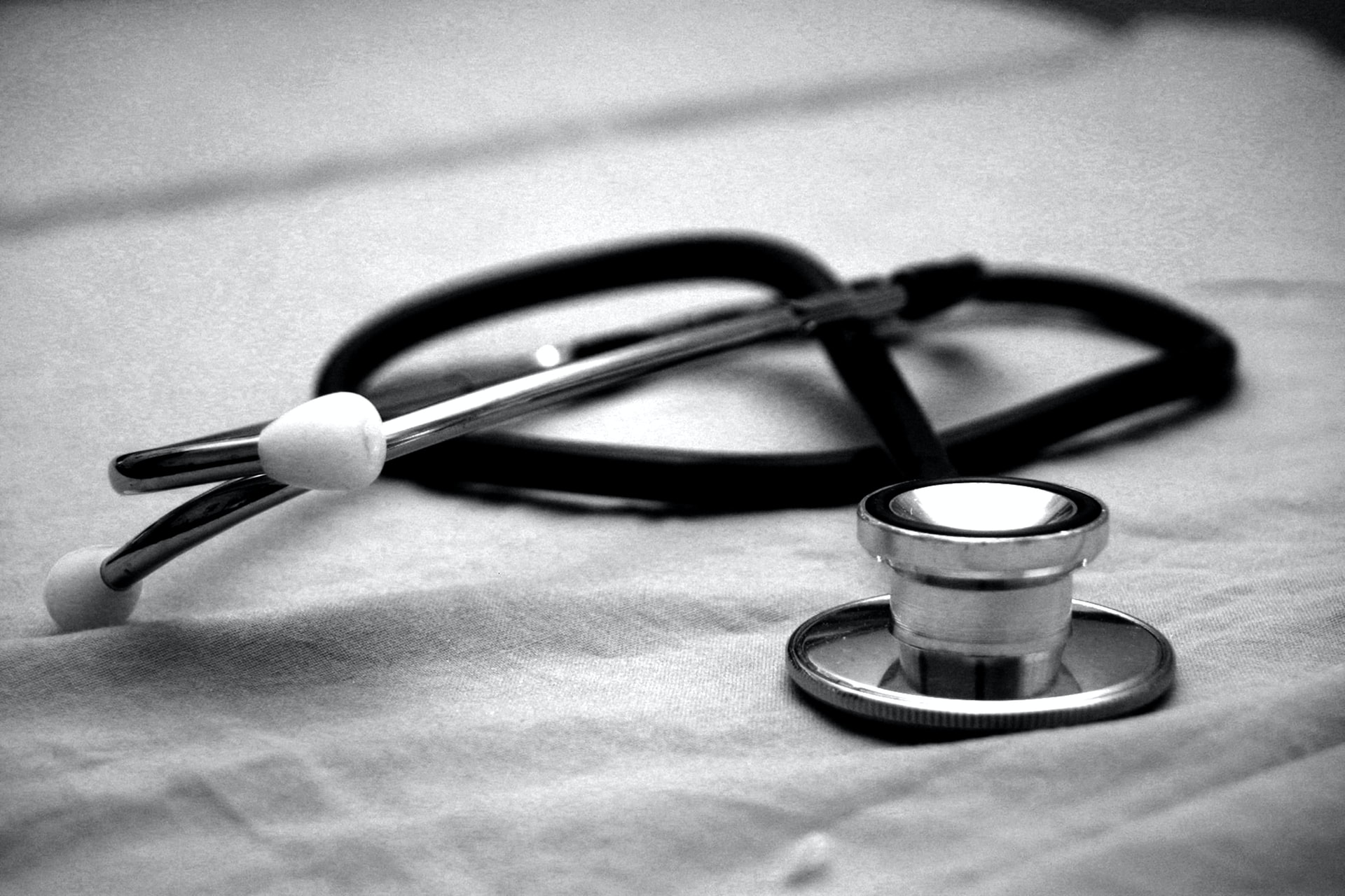 A stethoscope sits on a sheet, in black and white.