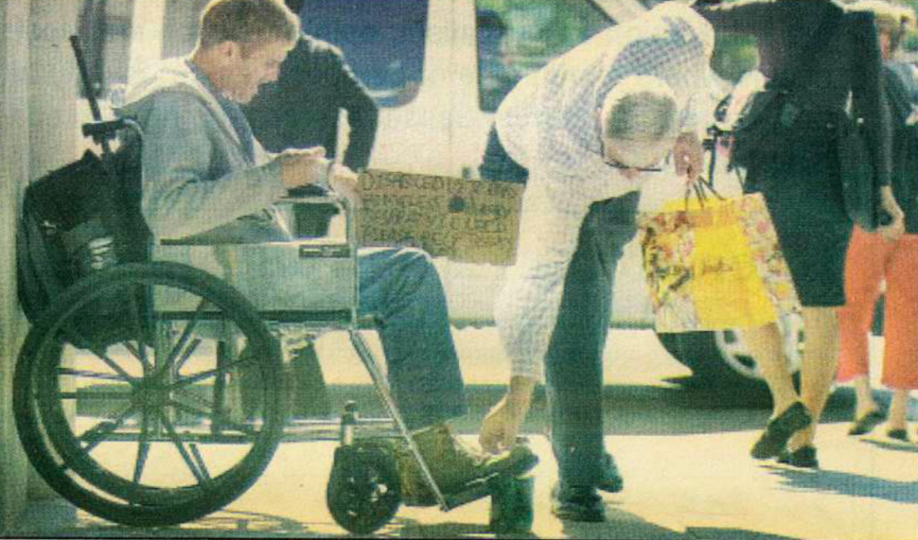 A passerby drops some loose change into the can of a man in a wheelchair.