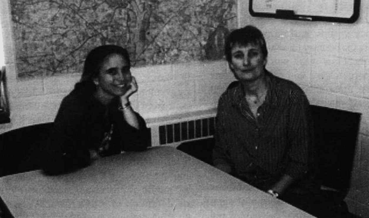 A photo of two women sitting a table and smiling at the camera.