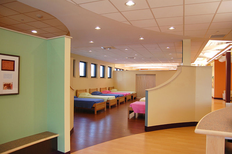 Multiple beds are lined up along the wall of a large room.