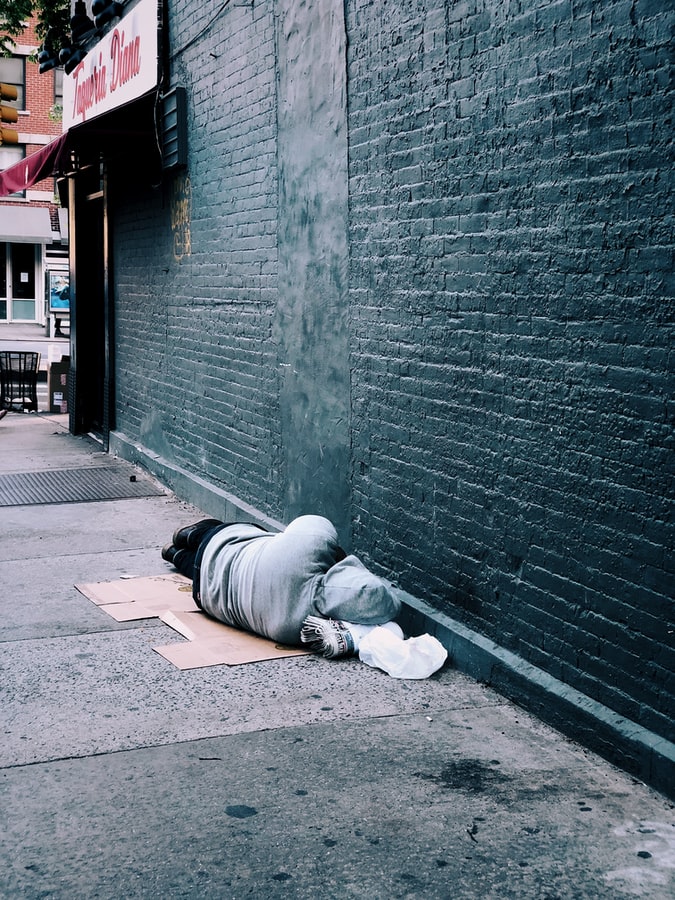 A person lies facing the wall of a building on the sidewalk.