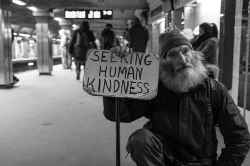 A man holds up a sign that says "Seeking Human Kindness."